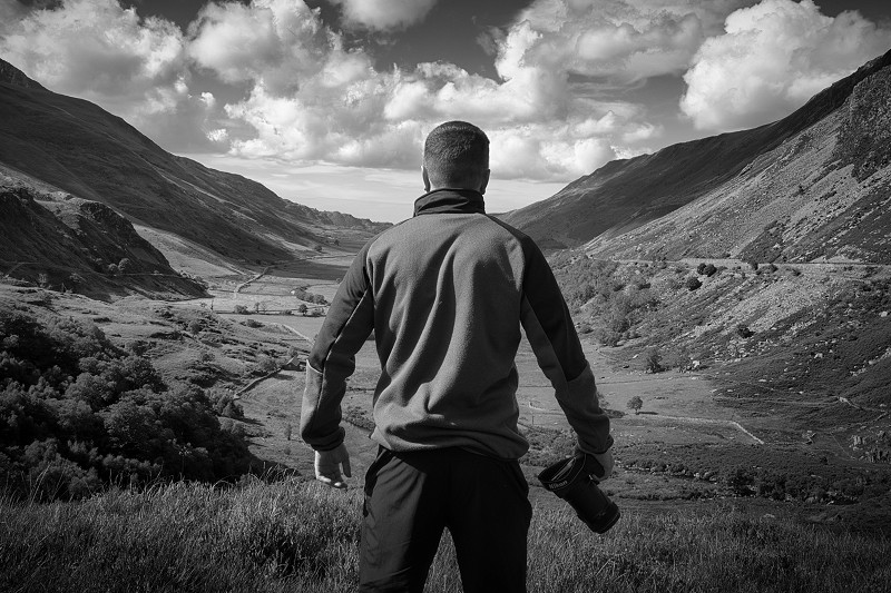 a sepia photo of a man with his back turned, standing in front of mountains